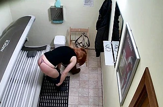 Red-haired naked girl obediently lies on tanning bed and absorbs rays