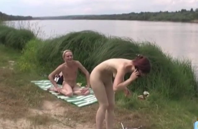 Friend of the naked man and red-haired girl films them outdoors