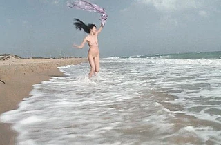 Happy brunette girl is in a mood to walk being naked on the beach
