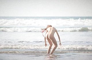 Naked girl in red headband walks on the beach making guys drool