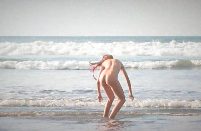 Naked girl in red headband walks on the beach making guys drool